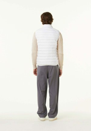 Witte puffer vest met een hoge kraag en horizontale stiksels. Draagt over een gestructureerde beige trui en gecombineerd met losse grijze broek.