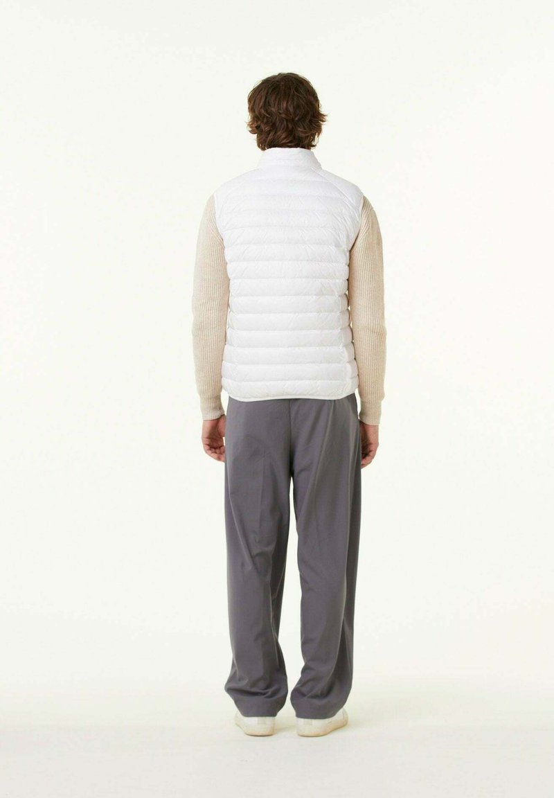 Witte puffer vest met een hoge kraag en horizontale stiksels. Draagt over een gestructureerde beige trui en gecombineerd met losse grijze broek.