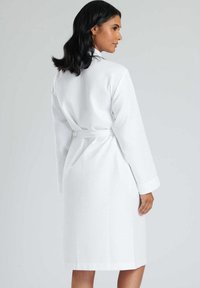 Accappatoio bianco a trama con maniche lunghe, cintura da annodare e tasche, caratterizzato da un motivo intessuto per un dettaglio visivo aggiuntivo.