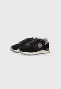 Schwarze Sneaker aus Wildleder und Mesh-Material. Mit einem runden Logo, grauen Akzenten und einer weißen Zwischensohle mit einer strukturierten Gummisohle.