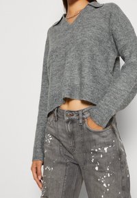 Grå, kort stickad tröja med V-ringning och krage, kombinerad med grå jeans som har färgfläckar och en avslappnad passform.