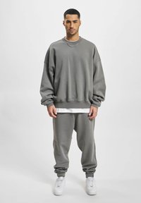 Overdimensioneret grå sweatshirt med ribbekanter ved ærmerne og kanten, parret med matchende tætsiddende svedbukser og hvide sneakers. Glat tekstur hele vejen igennem.