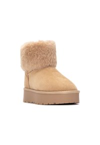 Botín de tobillo de ante marrón con un suave puño de piel sintética, punta redondeada y suela de goma plana con ranuras de tracción. Detalles de costura visibles.