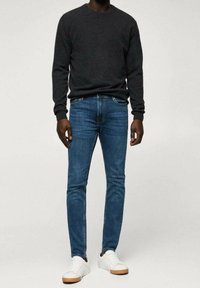 Tummanharmaa neulepaita, siniset pillifarkut ja valkoiset tennarit vaaleanruskeilla pohjilla. Asu on rento ja istuva.