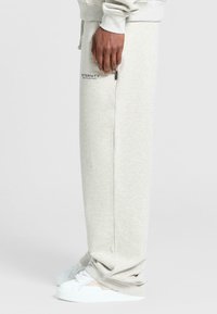 Helle graue Sweatpants mit lockerer Passform. Mit Seitentaschen und einem Logodruck. Kombiniert mit weißen Sneakers, was einen lässigen Look zeigt.