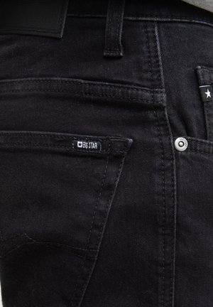 Czarne dżinsy o slim fit, z małą przednią kieszenią, widocznym przeszyciem i metką marki na tylnej kieszeni.