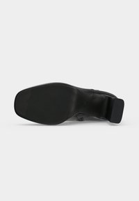 Semelle de chaussure en cuir noir avec un petit talon carré et une surface en caoutchouc texturée à l'avant et au talon pour une bonne adhérence.