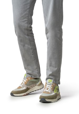 Grüner und brauner Sneaker mit Mesh- und Wildlederdesign, ausgestattet mit weißen Schnürsenkeln, gesprenkelter Sohle und Neon-Highlights. Getragen mit grauer Jeanshose.