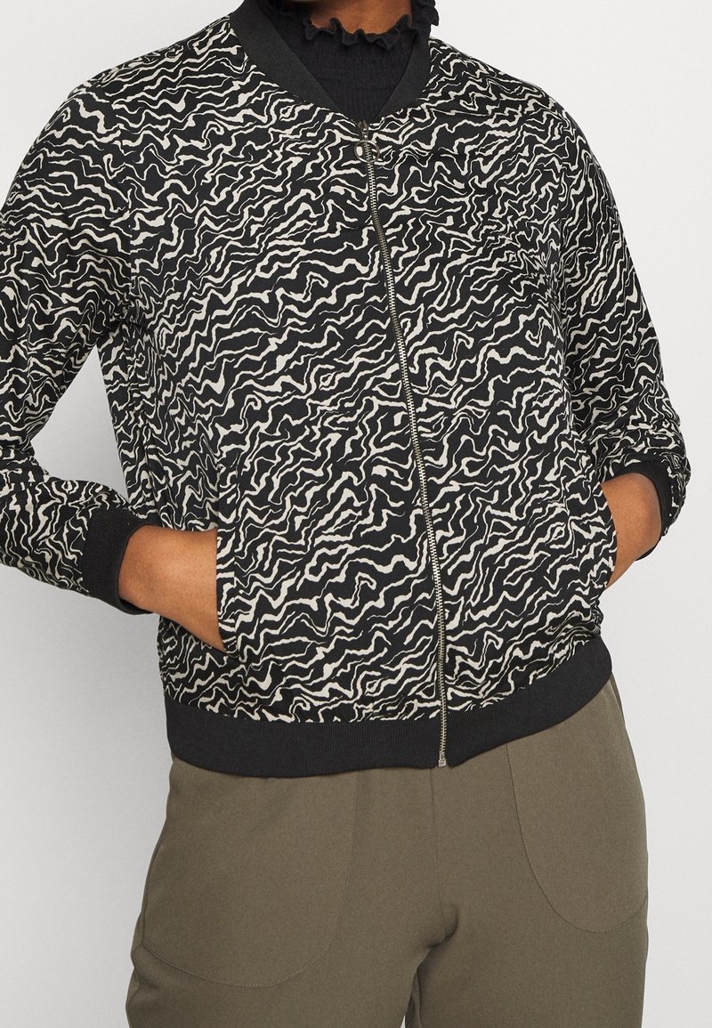 Bomber bunda s černobílým vzorem, se zipem v přední části, žebrovanými manžetami a spodním lemem, s vlnitým designem a uvolněným střihem.