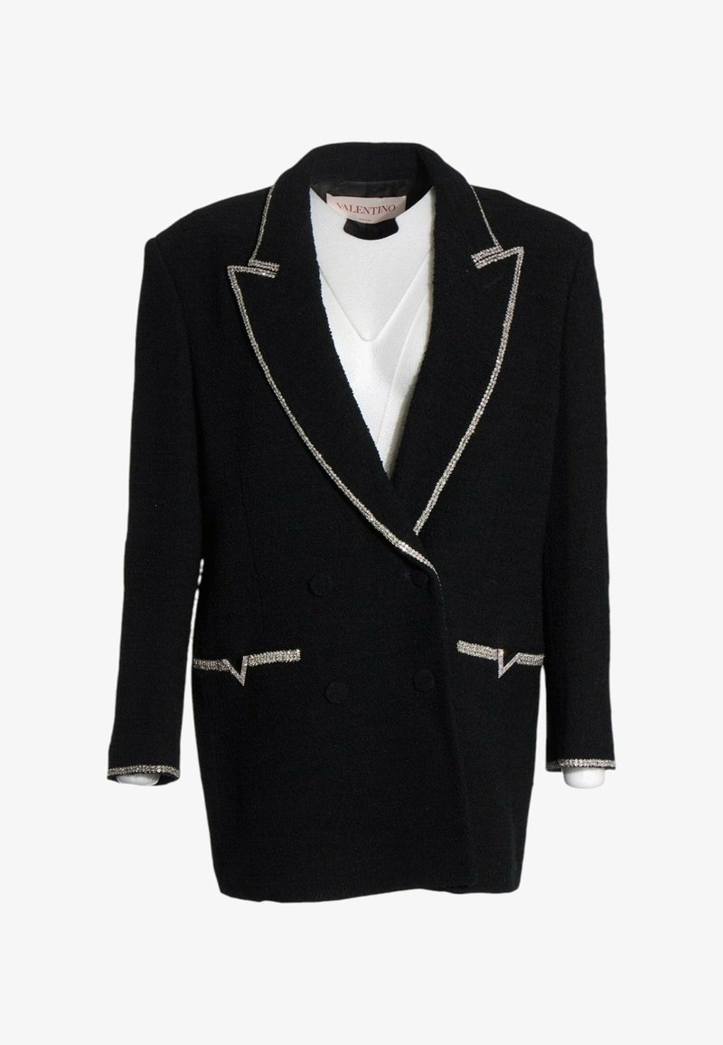 Blazer noir à double boutonnage avec bordure argentée sur les revers, poches et poignets, porté sur un top blanc, étiquette Valentino à l’intérieur du col.