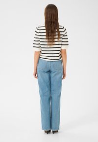 Pull en tricot noir et blanc à rayures, à manches courtes, associé à un jean droit taille haute bleu clair. Texture lisse avec des coutures visibles.