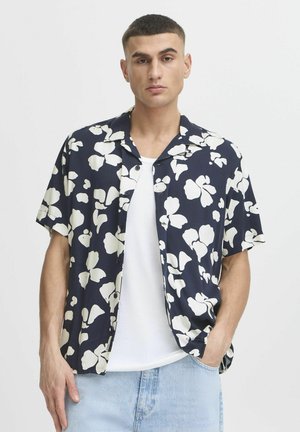 Short-sleeve button-up shirt in navy with large white floral pattern, featuring a camp collar and relaxed fit. Smooth fabric texture.