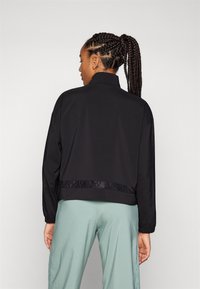 Chaqueta atlética negra con un alto cuello, mangas largas y una cintura texturizada. El diseño es simple y funcional, con un acabado suave.