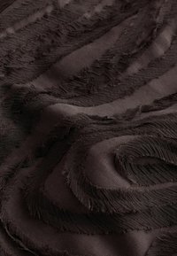 Tissu brun foncé avec des motifs ondulés irréguliers et en relief, créant une surface texturée en couches.