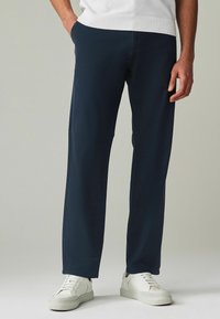 Pantaloni blu navy realizzati in tessuto morbido, con una vestibilità dritta e tasche laterali, abbinati a sneakers bianche.