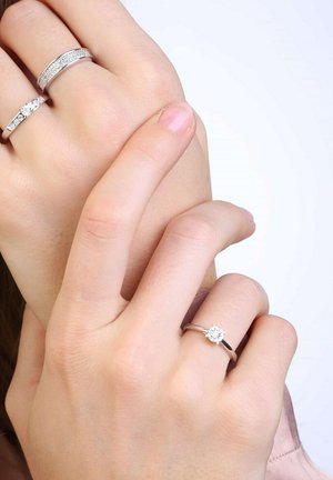 Drie ringen: een slanke gepolijste zilveren band, een bredere band met cubic zirconia accenten, en een solitaires ring met een ronde diamanten zetting.