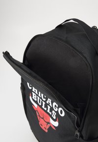 Crni ruksak s logom crvene bika i tekstom "CHICAGO BULLS", sa zatvaračem na patentni zatvarač i glatkom, teksturiranom unutrašnjošću.