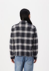 Plaid flannel jacket in navy and gray, textured fabric, collared design, straight cut, paired with light blue jeans.