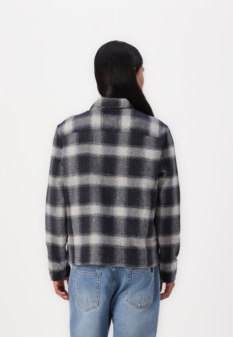 Karierte Flanelljacke in Marineblau und Grau, strukturierter Stoff, Kragen-Design, gerader Schnitt, kombiniert mit hellblauen Jeans.