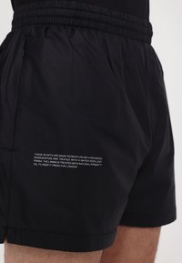 Black nylon shorts with an elastic waistband, featuring a water-repellent finish, and text detailing on the side.