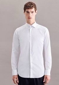 Camicia bianca a maniche lunghe con bottoni, colletto classico e orlo dritto. Realizzata in un tessuto liscio con una trama sottile.