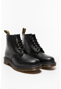 Botas de cuero negro hasta el tobillo con punta redondeada, diseño con cordones, lengüeta amarilla y suela de goma rugged con relieve texturizado.
