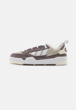 Zapatillas marrones y crema con materiales de nobuck y malla, que presentan rayas blancas, diseño de cordones y una suela de goma con detalles texturizados.