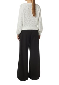 White patterned knit sweater with open diamond design and long sleeves paired with loose-fitting black pants. Smooth texture, relaxed fit.