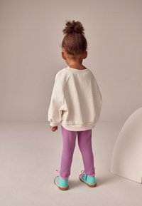 Felpa oversize grigio chiaro, leggings viola e scarpe da ginnastica multicolori con suola in gomma, caratterizzate da accenti giocosi.