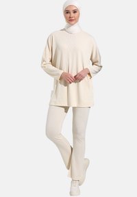 Beige geribbelde top met lange mouwen, gecombineerd met bijpassende geribbelde broek. De outfit heeft een comfortabele pasvorm en is gemaakt van een zachte stof.