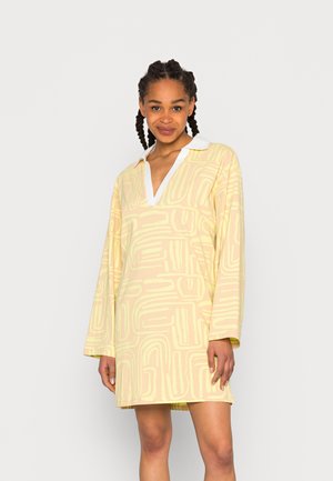 Vestido de mangas curtas em amarelo pálido com colarinho branco, apresentando um padrão de linhas abstratas e um corte solto, feito de tecido macio.
