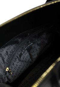 Black handbag interior with a zippered pocket. Features a smooth texture and gold-tone hardware, with a repeating logo pattern on fabric.