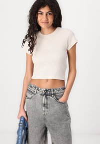 Beige prúžkovaný crop top s krátkymi rukávmi, so malým bielym logom. V kombinácii s vyšším pásom, vyblednutými šedými džínsami.