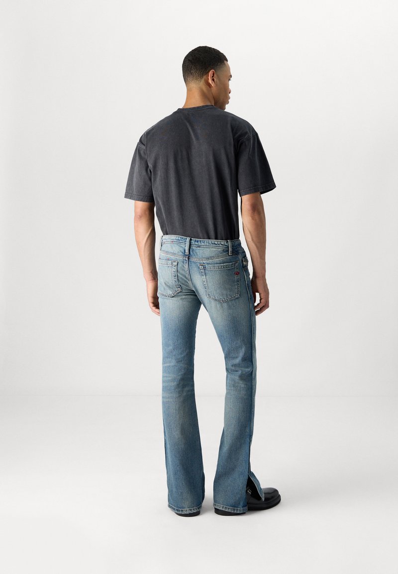 Dunkelgraues T-Shirt kombiniert mit hellblauen, ausgestellten Jeans, die seitliche Schlitze und Gesäßtaschen haben. Das Model steht mit dem Rücken zur Kamera.