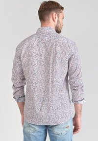 Camicia con motivo floreale in tessuto leggero, caratterizzata da tonalità di bianco, blu e rosso. Maniche lunghe con polsini abbottonati, design del colletto classico.