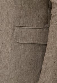 Brauner Leinenblazer mit strukturiertem Finish, ausgestattet mit einer seitlichen Tasche und einer taillierten Passform. Gestickte Details entlang der Nähte.