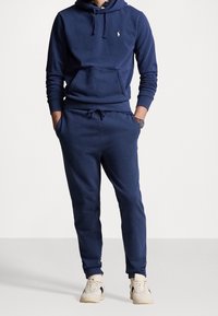 Mörkblå huvtröja med kenguruficka och dragsko, matchad med joggingbyxor i samma tyg. Båda är gjorda av mjukt, texturerat tyg.