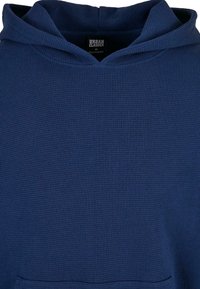 Mørk blå hettegenser med teksturert vaffelstrikket stoff, snøre i hetta og kengurulomme. Merket angir størrelse M, merke Urban Classics.