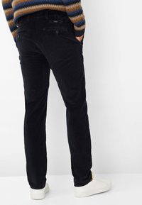 Zwarte corduroy broek met een rechte pasvorm, voorzien van achterzakken en een subtiele ribbelstructuur. Gecombineerd met witte sneakers.