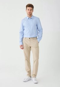 Ljusblå skjorta med knappar, beige byxor och vita sneakers. Skjortan har en slät textur; byxorna är skräddarsydda med en vanlig passform.