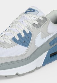 Λευκά και ανοιχτό γκρι sneakers Nike Air Max με μπλε λεπτομέρειες, λευκά κορδόνια και ορατή αερόσολα στη σόλα.