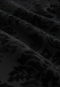 Tisu negru cu un model floral texturat, având designuri în relief. Textură netedă cu un luciu subtil, evidențiată de plisuri și umbre.