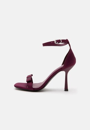 High-heeled open-toe sandal in dark purple with ankle strap and front bow detail, displayed on a white background.