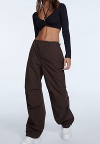 Bruine cargobroek met een losse pasvorm, voorzien van zijzakken en een elastische tailleband. Gepaard met een zwarte lange mouw crop-top.