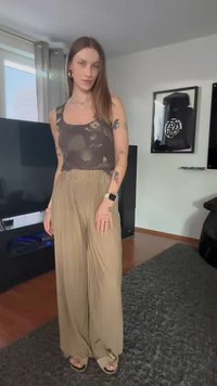 Leichte, beige Plissee-Hose mit hoher Taille und lockerer Passform, kombiniert mit einem dunklen, gemusterten Tanktop und flachen Sandalen.