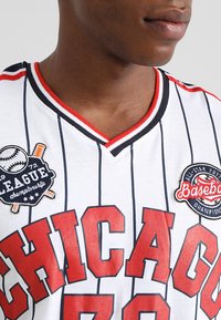 Baseballtrøje med røde og sorte detaljer, lodrette hvide striber, V-hals design, med broderede patches med holdlogoer.
