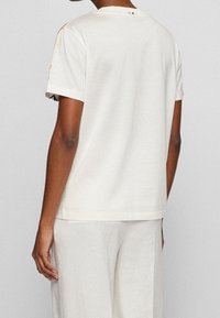 Camiseta de manga corta en color crema con un corte relajado, que presenta un gráfico sutil en el hombro y una textura suave y lisa.
