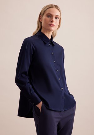 Navyblauw overhemd met lange mouwen, een kraag en knopen aan de voorkant, met zijsplitten. Gemaakt van een gladde stof en een losse pasvorm.