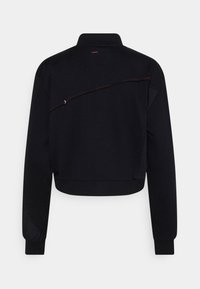 Veste courte noire à manches longues avec col haut et couture diagonale rouge dans le dos.
