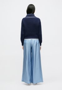 Lahealt sinine soonikkoes kampsun laia sallkraega, mida täiendab helesinised satiinist laiade pükstega, millel on külgtriip ja sile tekstuur.